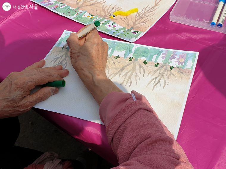 어르신이 예시로 제공된 그림을 보면서 꽃을 그려넣고 있다.