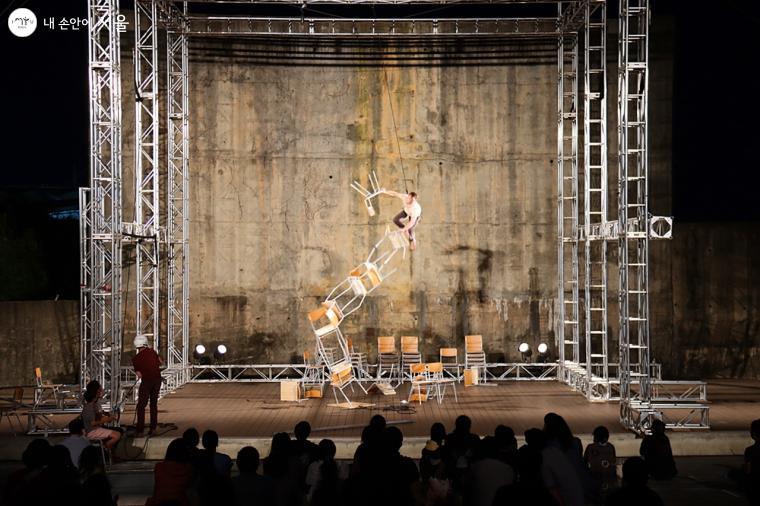 갈라피아 서커스의 '사람의 기초' 공연. 켜켜이 쌓인 의자 위를 아슬아슬하게 올라가는 예술가의 모습을 숨죽여 지켜보는 관객들