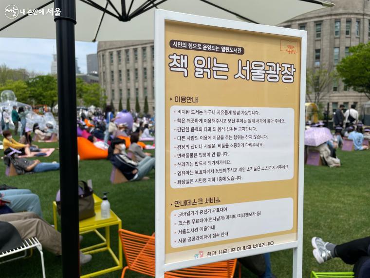 책읽는 서울광장 이용안내 표지판 뒤로 광장을 여유롭게 즐기고 있는 시민들의 모습이 보인다 