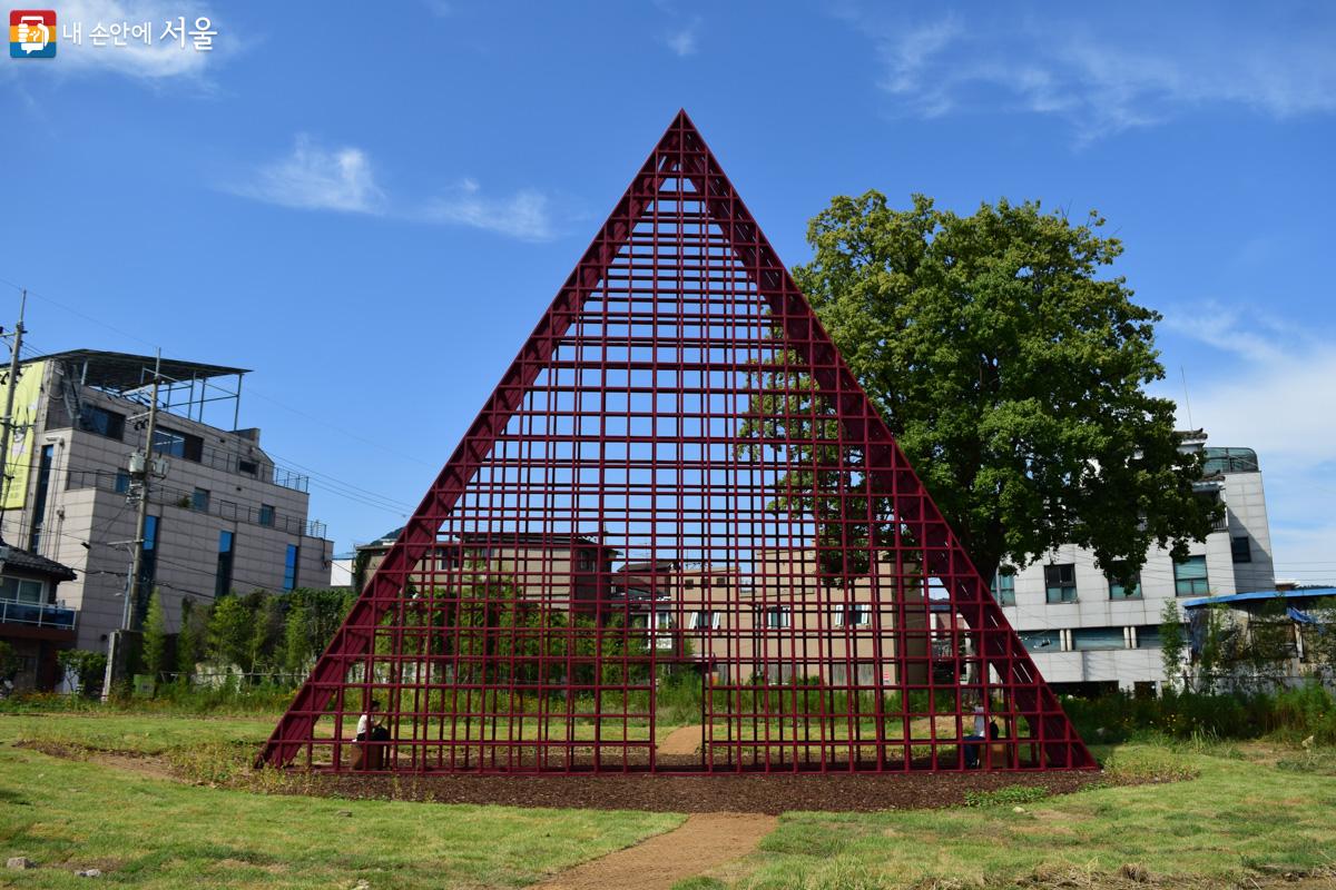 '현장프로젝트' 작품 일부로 페소 본 에릭사우센이 제작한 <페어 파빌리온>. 거대한 빨간색 정삼각형 구조물. 삼각형 내부 양끝에 하나씩 의자가 놓여 있다. ©이명은