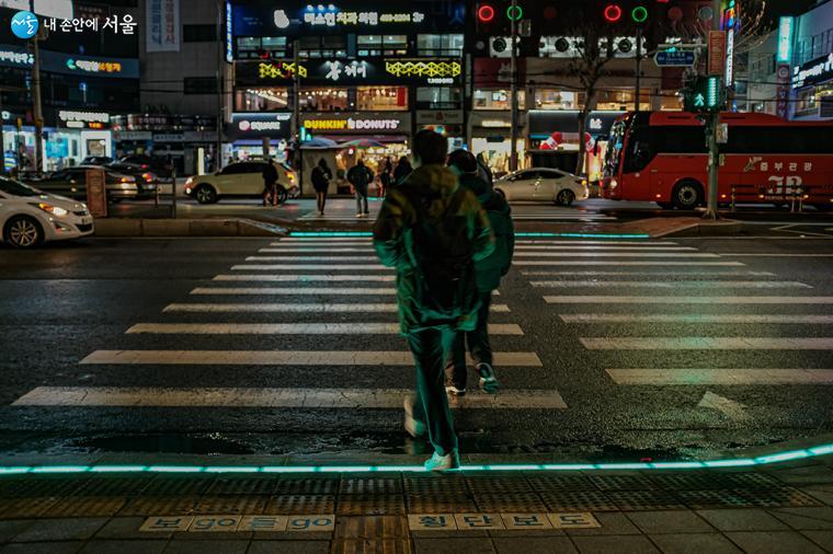 아차산역 바닥 신호등 LED 패널이 녹색으로 바뀌어 시민들이 신호를 건너는 모습.