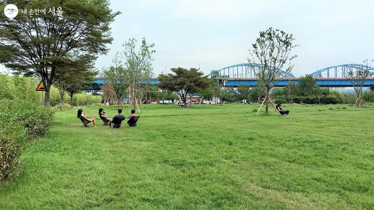 공원 널따란 잔디마당에서 시민들이 여가와 휴식을 만끽하고 있다. 배경으로 새롭게 심은 나무들과 동작대교가 보인다. 