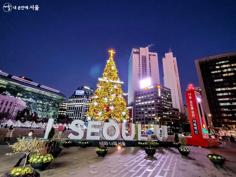 서울 도심 빌딩 숲을 배경으로 화려하게 빛나는 성탄 트리와 서울광장 야경.  
