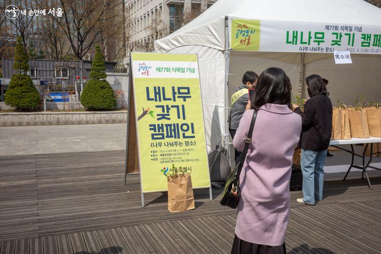 캠페인 안내판을 배경으로 나무 인증샷을 찍는 한 시민의 모습