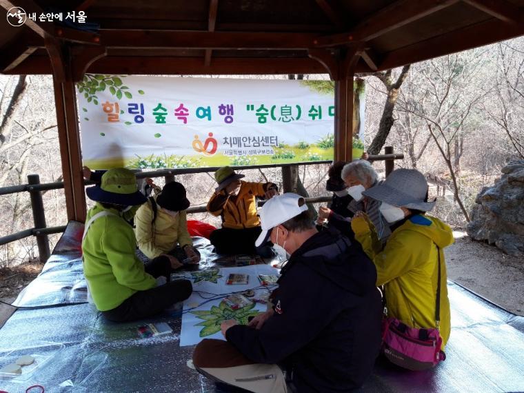 치매 어르신들이 힐링 숲속에서 즐겁게 꽃 그리기를 하고 있다.