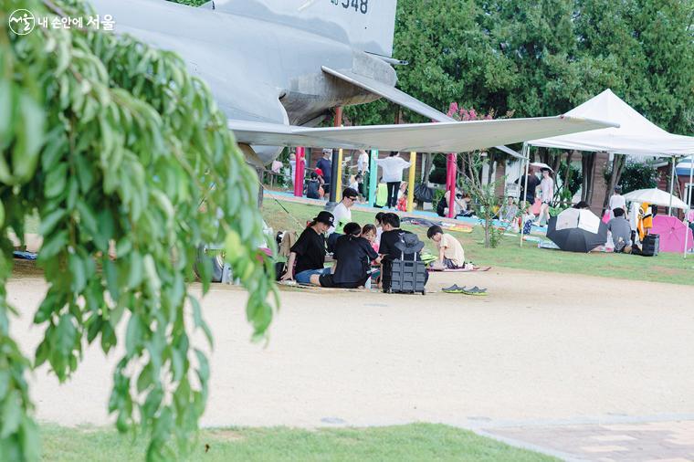 에어파크 비행기 아래 그늘에 가족단위로 돗자리를 펴고 더위를 피해 쉬고 있는 시민들이 보인다.