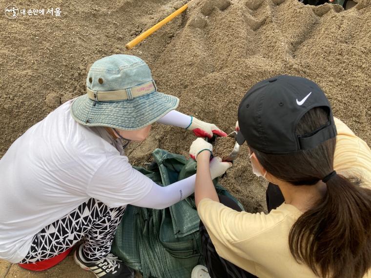 한 명은 모래주머니 입구를 벌리고, 한 명은 삽으로 모래를 퍼 담는다. ⓒ전주영