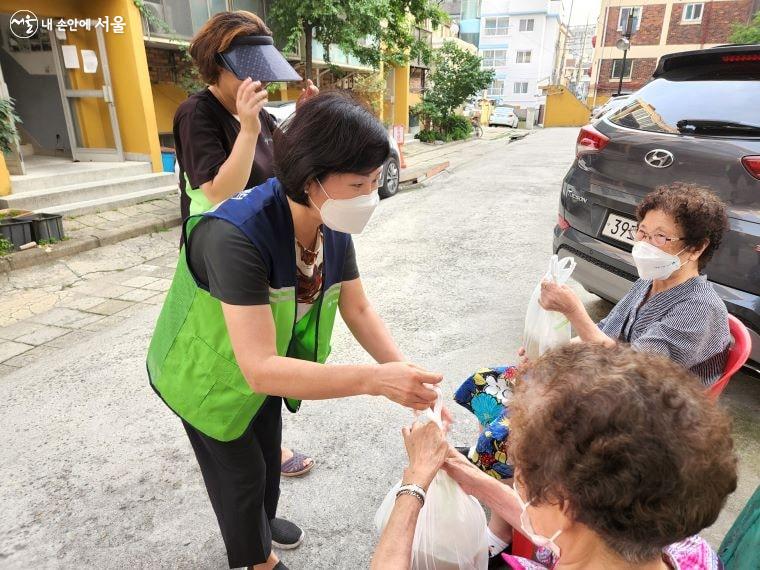 자원봉사자가 어르신에게 삼계탕을 전달하면서 인사를 건네고 있다.