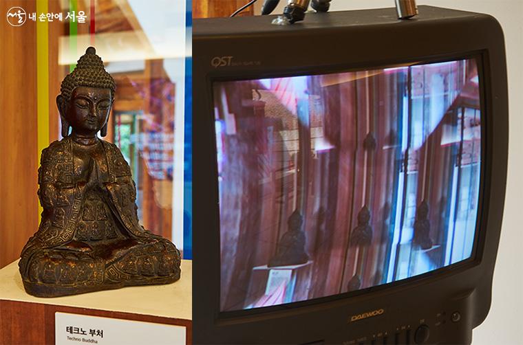 뉴욕 미술계에 큰 반향을 일으켰던 백남준의 작품 ‘TV 부처’를 오마주한 ‘테크노 부처’(김상돈 작가)의 모습. ‘TV 부처’에서 부처는 카메라로 촬영되는 자신의 모습이 실시간으로 상영되는 TV 화면을 바라본다 ⓒ이정규