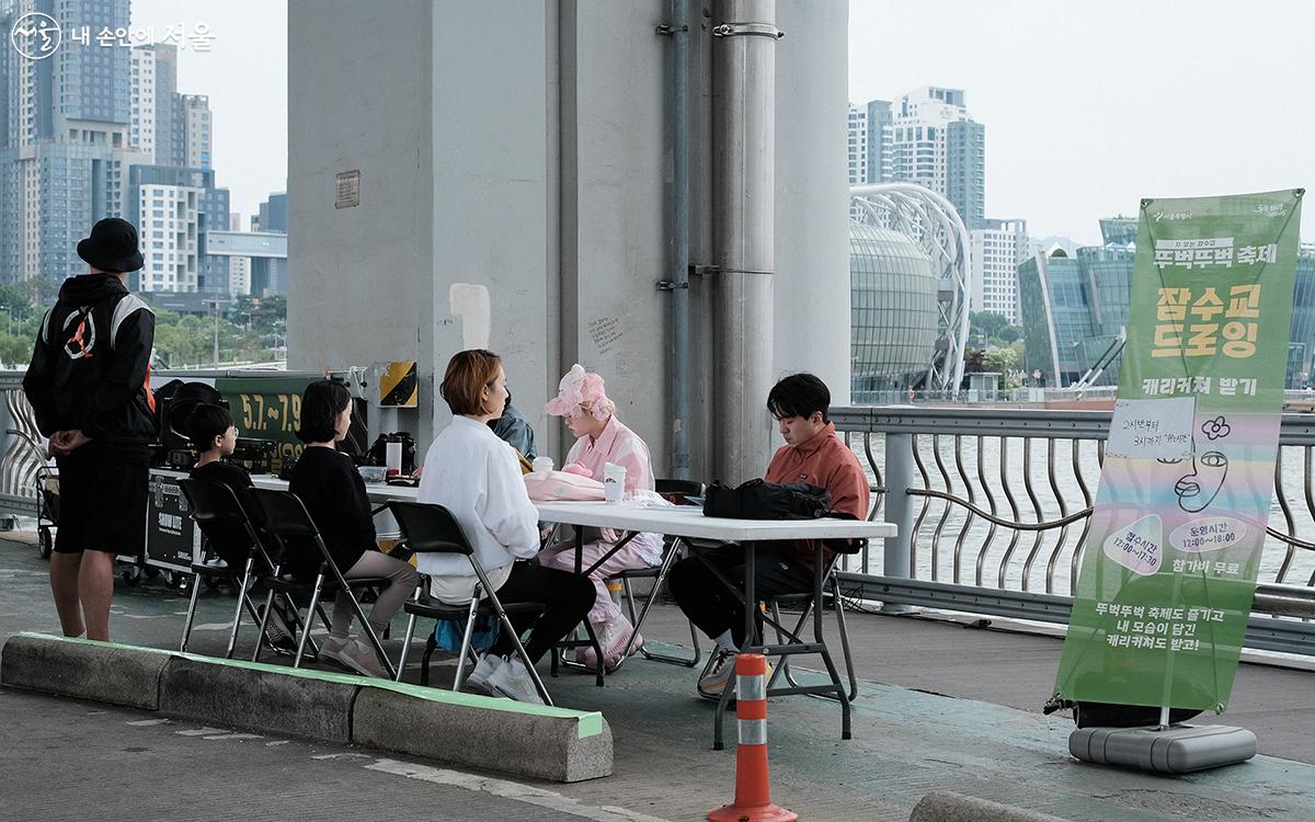 색다른 내 모습이 담긴 캐리커쳐를 선물 받을 수 있는 ‘잠수교 드로잉’을 체험하는 시민들 ⓒ김아름