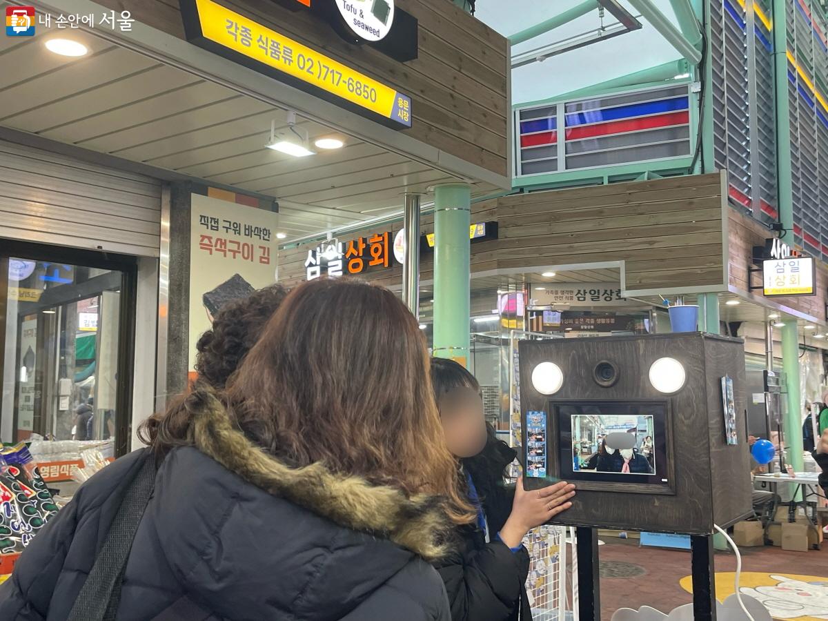 용문시장 캐릭터 용용이가 그려진 ‘용용3컷 인증샷’ 부스 앞에서 사진 촬영 중인 방문객들 ©이정민