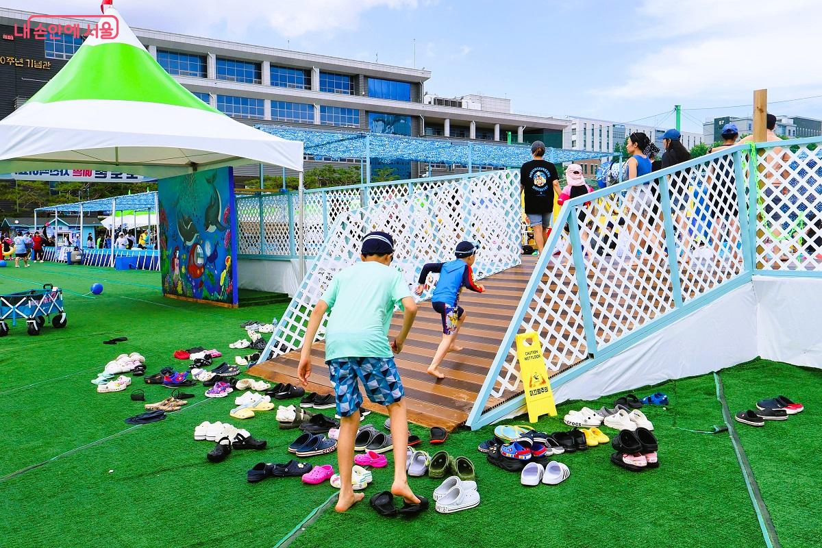 어린이들이 물놀이장에 빨리 들어가기 위해 신발을 벗자마자 신나게 뛰고 있다.