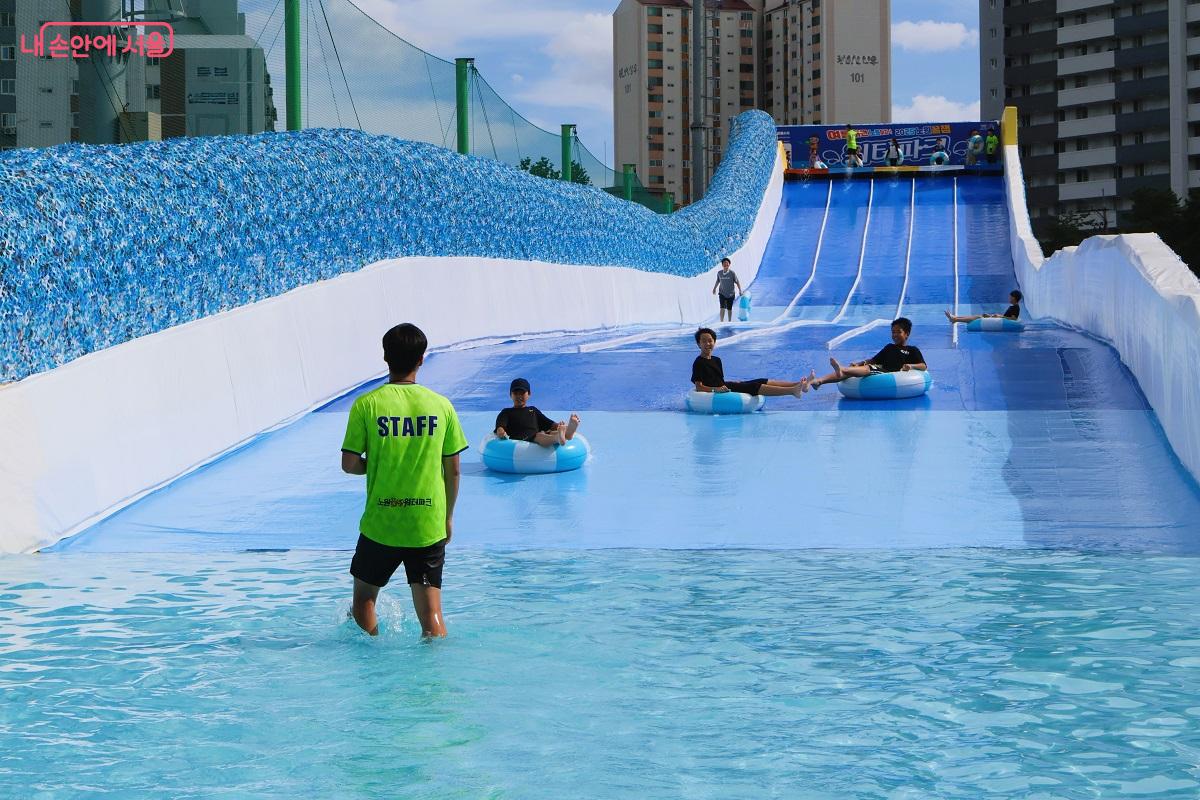 여름 방학을 맞은 어린이들이 100M 길이 워터슬라이드를 내려오며 환호를 지르고 있다.