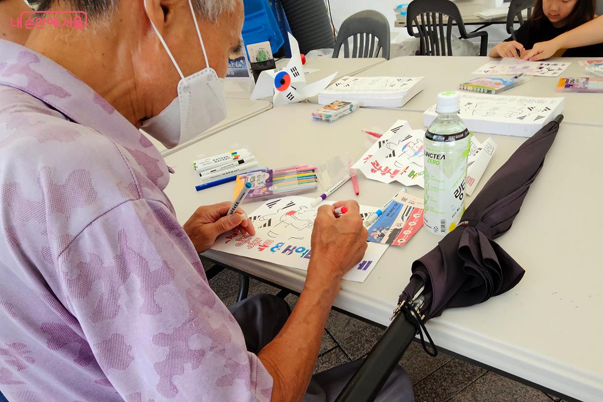 한 참가자가 마카펜으로 태극 문양과 해치 그림에 자신만의 문구와 색을 더하며, 광복의 의미를 담은 ‘태극기 해치 그리기’에 열중하고 있다. ©정향선