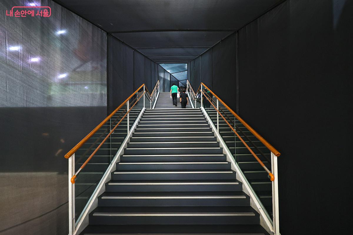 2층으로 오르는 계단. 전시장 내 이동 동선 공간들은 모두 검은색 천으로 둘러싸여 있다. ©김주연