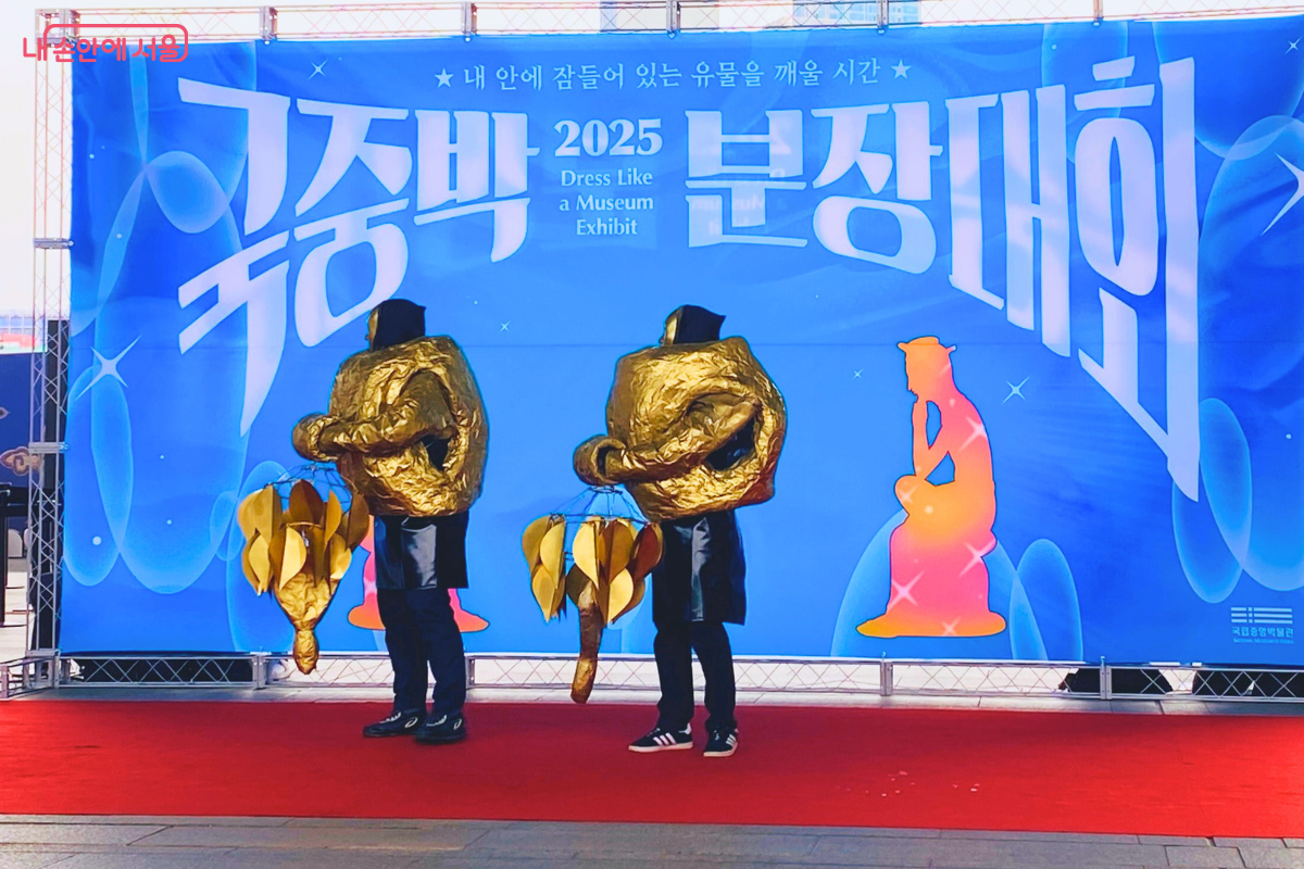 '경주 황오동 금귀걸이'로 분장한 '귀에 걸면 귀걸이' 팀 참가자 두 명이 무대 위에서 퍼포먼스를 하고 있다. 두 사람은 금색의 커다란 귀걸이 모양 의상을 입고 있다. ©양정화