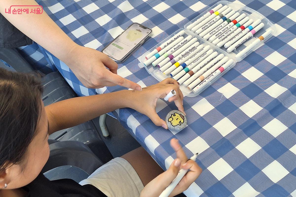 조약돌에 무지개색 마카펜으로 나만의 ‘정원을 여행하는 돌’ 을 새겨넣는 어린이의 모습