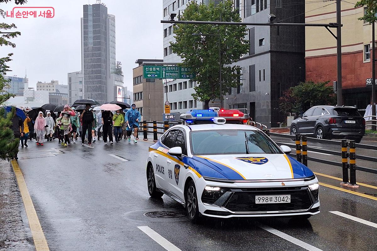 행렬의 앞에서 경찰차가 서행하며 안전한 행진을 이끌고 있다.