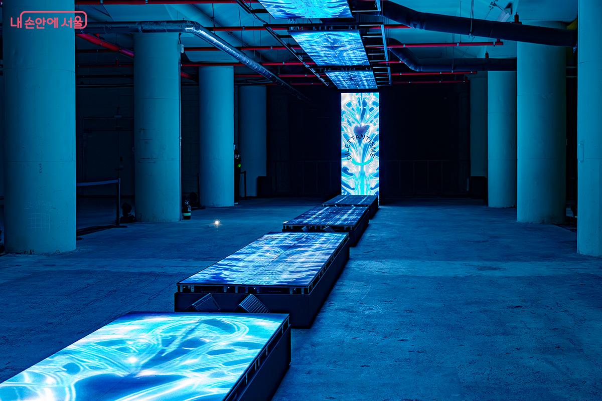 전시 공간 내부는 강렬한 네온 그린과 마젠타, 블루 조명이 공간 전체를 감싸며 SF 영화 속 한 장면을 연상시켰다. ©문청야
