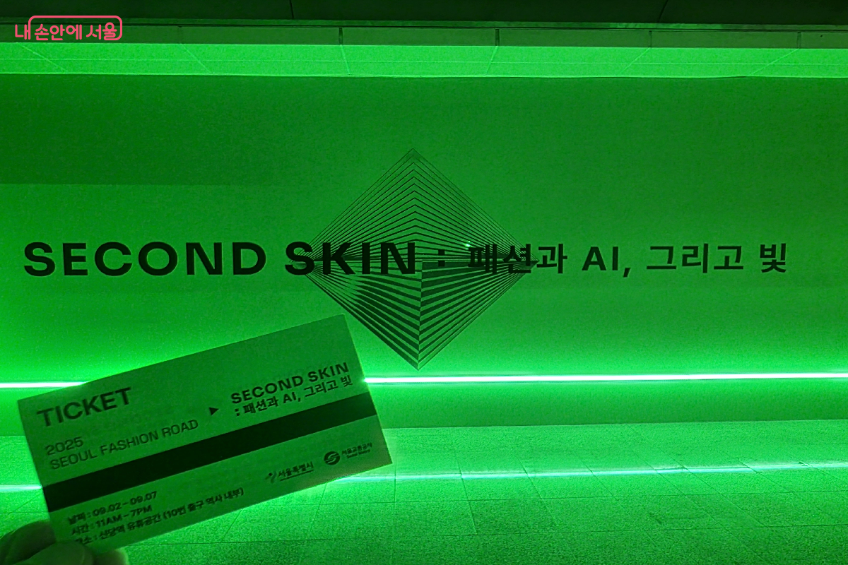 전시 로고가 들어간 전시 제목 앞에서 티켓을 들어 보인 모습 &copy;구정숙