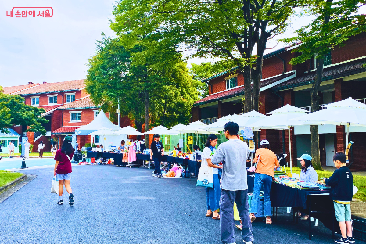 플리마켓 존의 모습. 하얀 파라솔 아래 여러 판매자들이 직접 만든 수공예품이나 다양한 물건을 진열해놓고 판매하고 있으며, 시민들이 구경하고 있다. ©양정화