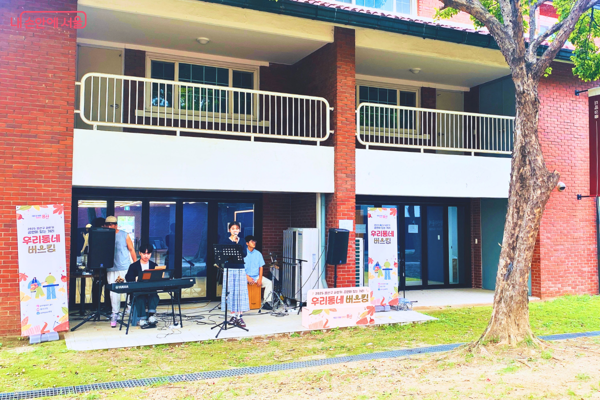 붉은 벽돌 건물 앞에서 '우리동네 버스킹' 팀이 공연을 하고 있다. 키보드 연주자와 여성 보컬이 중심이 되어 감미로운 라이브 음악을 선보이고 있다. ©양정화