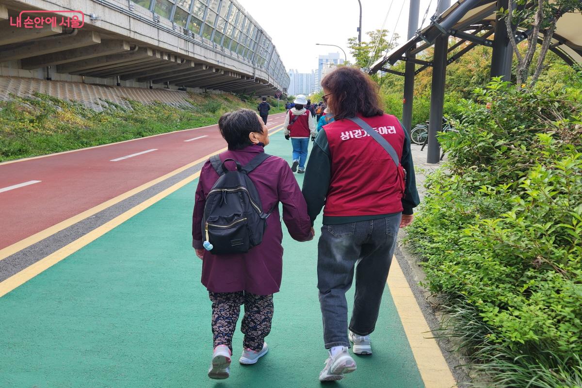 걷기 동아리 회원이 어르신의 느린 걸음걸이에 맞춰서 천천히 걷고 있다. ⓒ윤혜숙