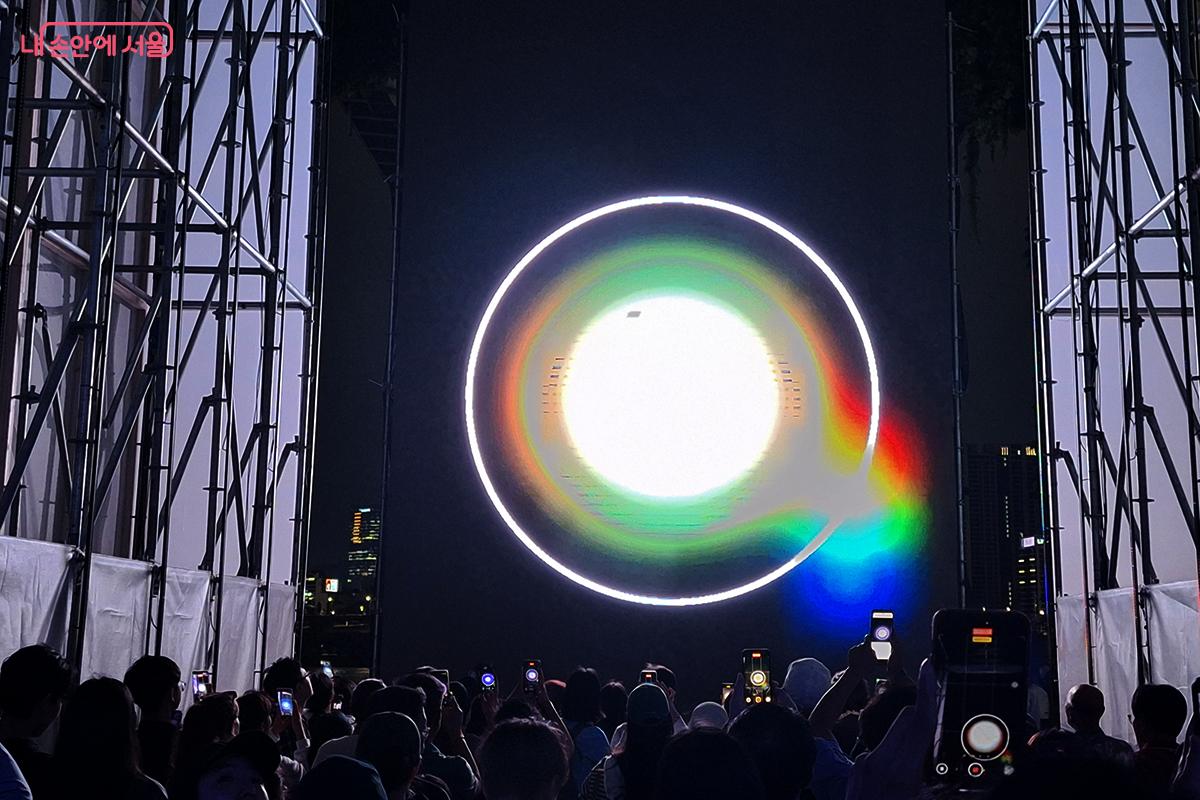 거대한 화면 위로 레이저가 흘러드는 순간 차갑던 콘크리트가 살아 움직이며 공간은 거대한 빛의 파도에 잠긴다. 