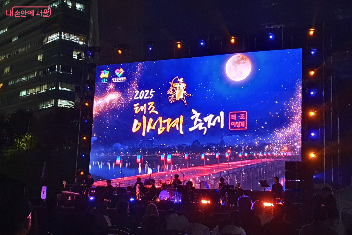 '2025 태조 이성계 축제'가 열리는 메인 무대의 모습. 대형 스크린에 보름달과 함께 축제 공식 로고가 선명하게 떠 있고, 무대 위에는 남기문 국악단이 연주를 준비하고 있다.