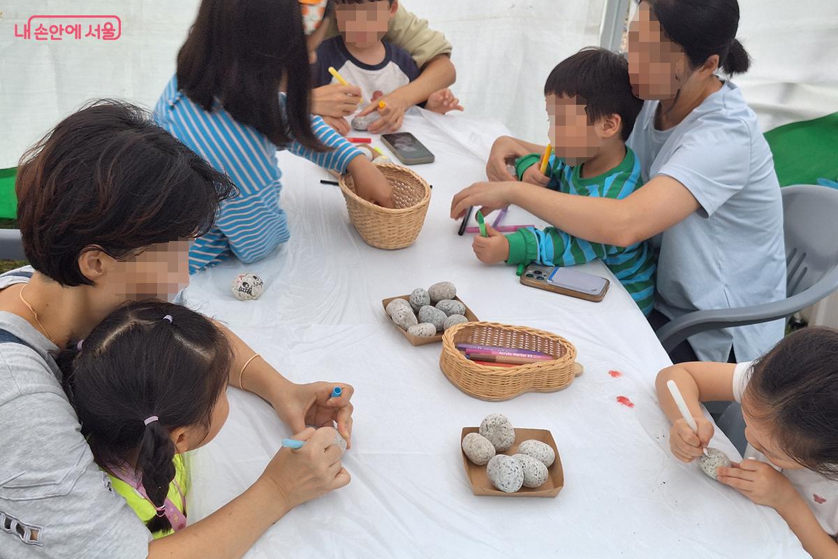 '정원을 여행하는 돌' 부스에서 아이들과 부모가 마카펜을 이용해 조약돌 위에 알록달록한 정원 돌을 만들고 있다. ©이혜숙