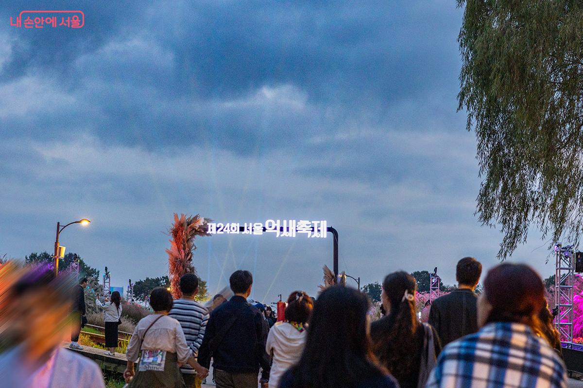 하늘공원 입구에 설치된 ‘서울억새축제’ 조형물 아래로 시민들이 저녁 산책을 즐기며 축제장을 향하고 있다. ⓒ장신자