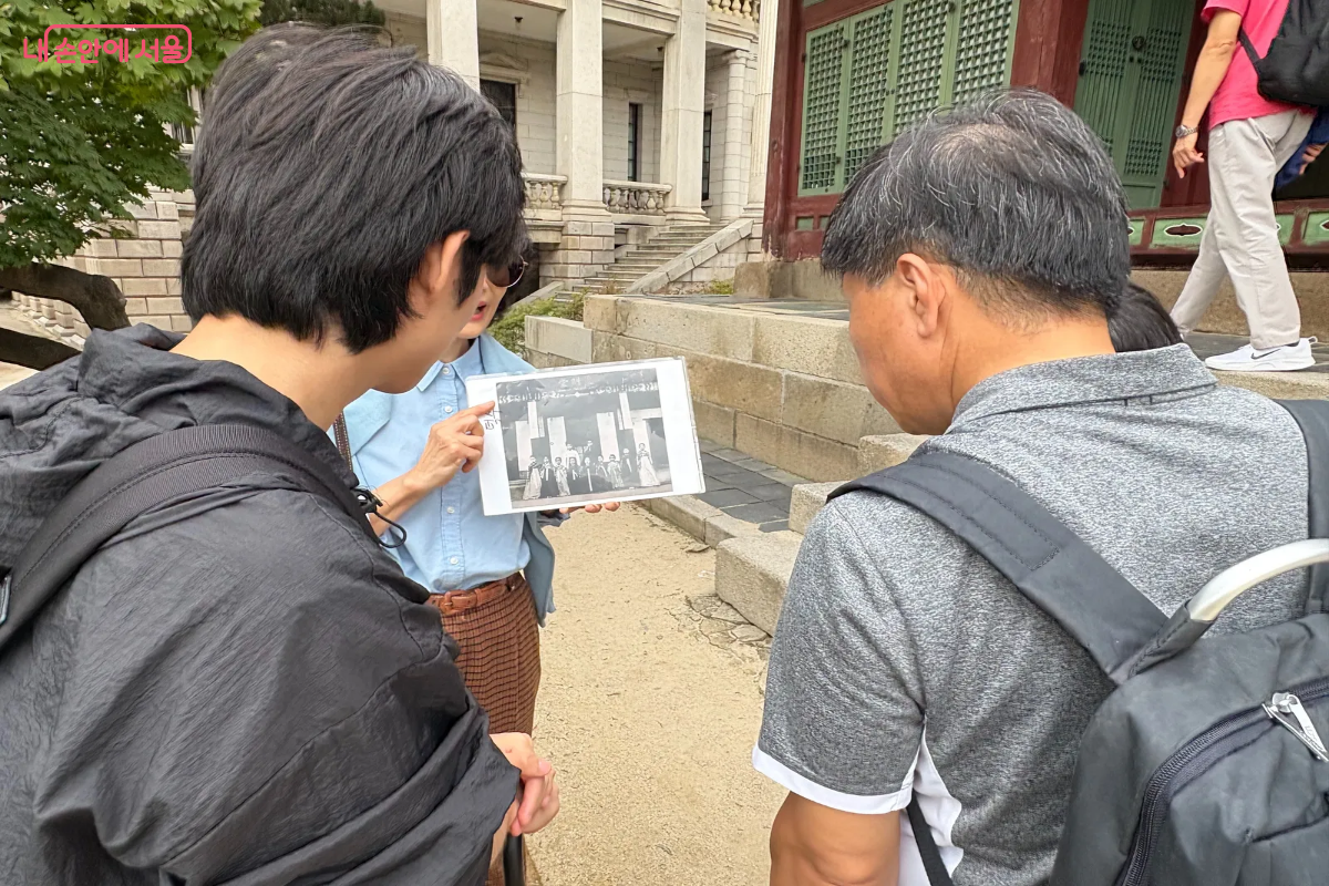 해설사가 덕혜옹주가 유치원에 다니던 과거 사진을 보여주며 준명당의 역사를 설명하고 있다. 참가자 2명이 해설을 열심히 듣고 있다. ©이혜린