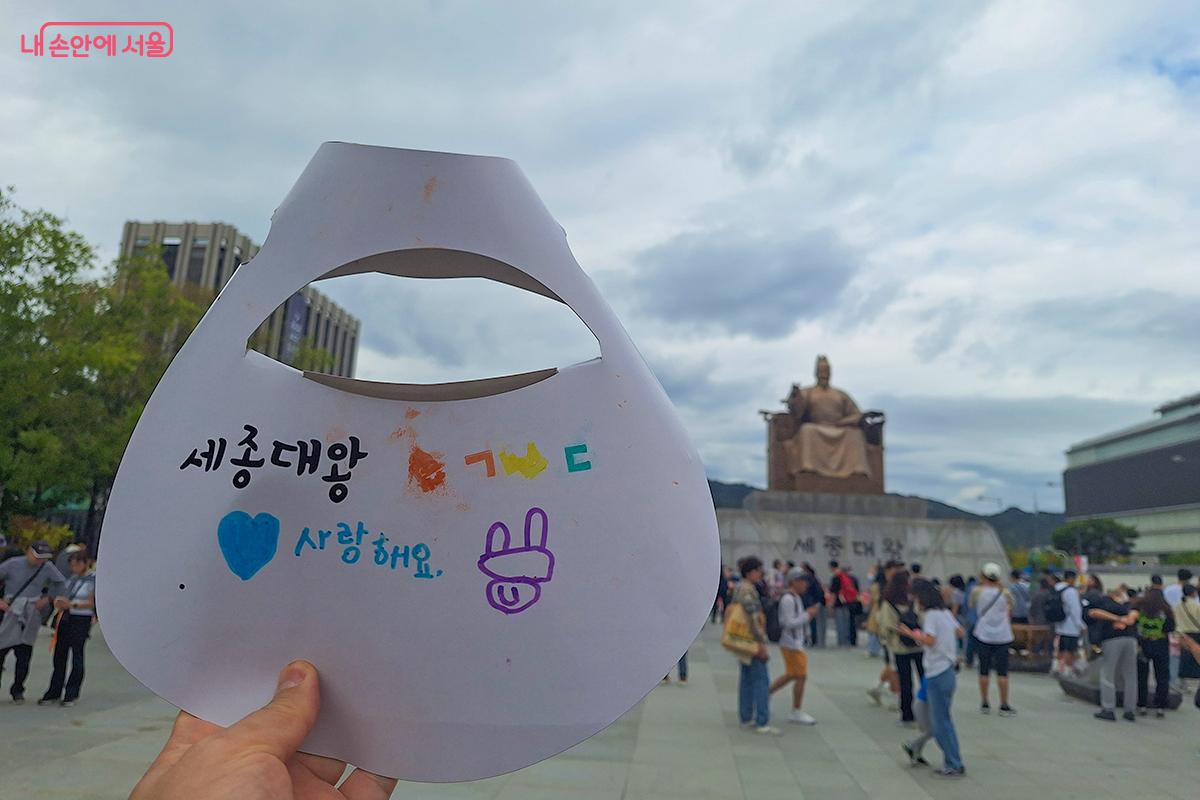 세종대왕 동상 앞에서 직접 만든 종이 모자를 들고 포즈를 취하고 있다. ©백승훈
