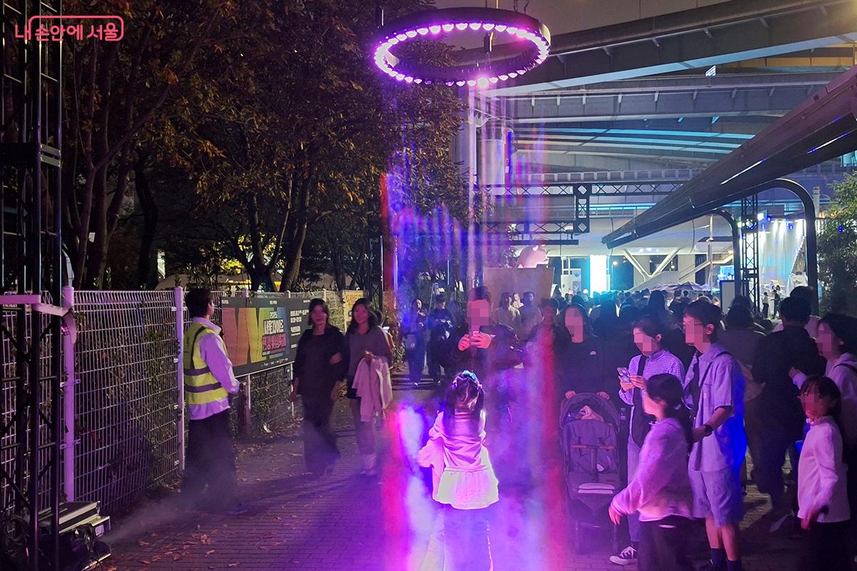 UFO 처럼 내려오는 LED 조명 아래에서 사진을 찍으며 즐거워하는 어린이들의 모습