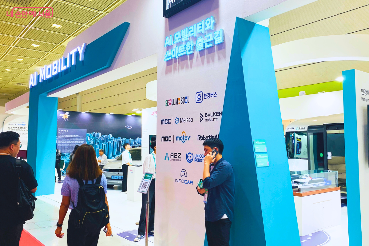  'AI 모빌리티와 스마트한 출근길'이라는 문구가 적힌 'AI 모빌리티'관 입구. 많은 관람객들이 부스 안을 오가며 자율주행차, 차세대 대중교통 시스템 등 미래 이동 수단과 관련된 첨단 기술들을 살펴보고 있다.
