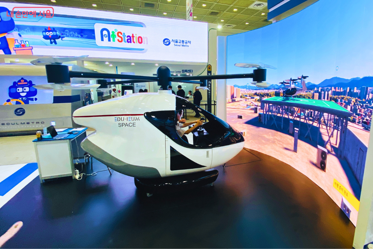 한 시민이 도심항공교통(UAM) 시뮬레이터에 탑승해 조종 체험을 하고 있다. 전면의 대형 스크린에는 도심 상공을 비행하는 그래픽이 생생하게 펼쳐져 미래 모빌리티를 현실처럼 경험하게 한다.