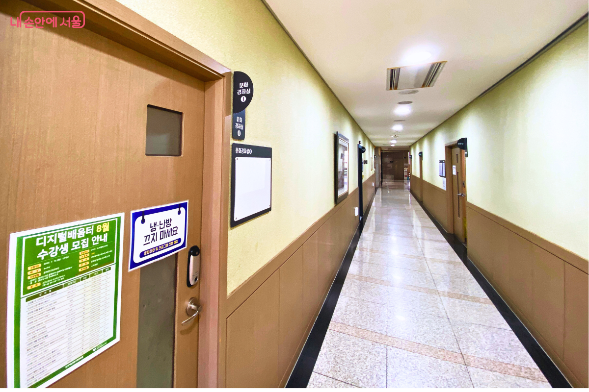 4층 문화강좌실로 향하는 긴 복도의 모습이다. 왼쪽의 닫힌 문에는 '디지털배움터 8월 수강생 모집 안내'라고 쓰인 녹색 포스터와 '냉·난방 끄지 마세요'라는 파란색 안내문이 붙어 있다. ©양정화