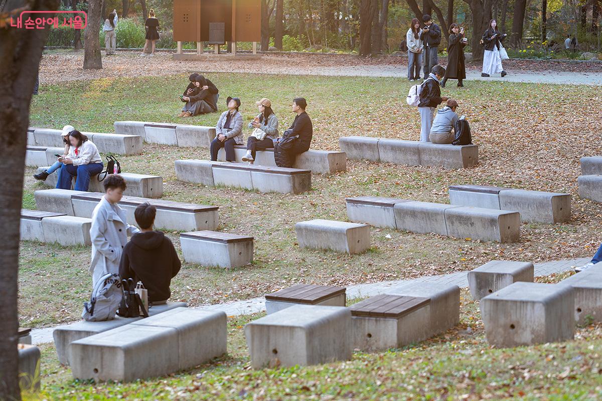 가을빛으로 물든 나무들 사이, 벤치에 앉아 대화를 나누거나 산책을 즐기는 시민들의 모습 ©문청야
