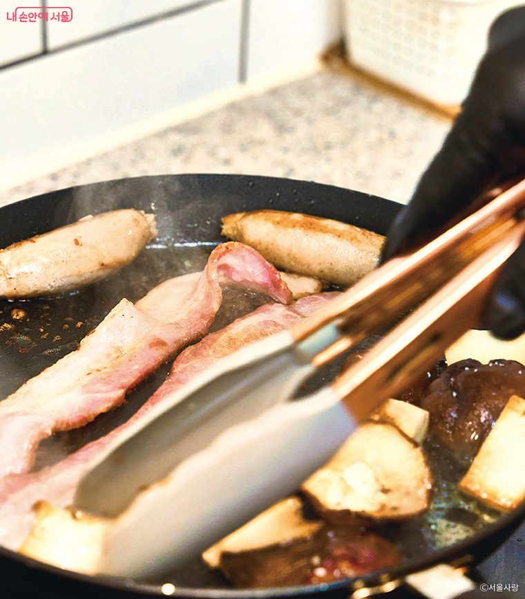 노쉬 브렉퍼스트를 위한 생소시지와 베이컨을 굽는 장면.