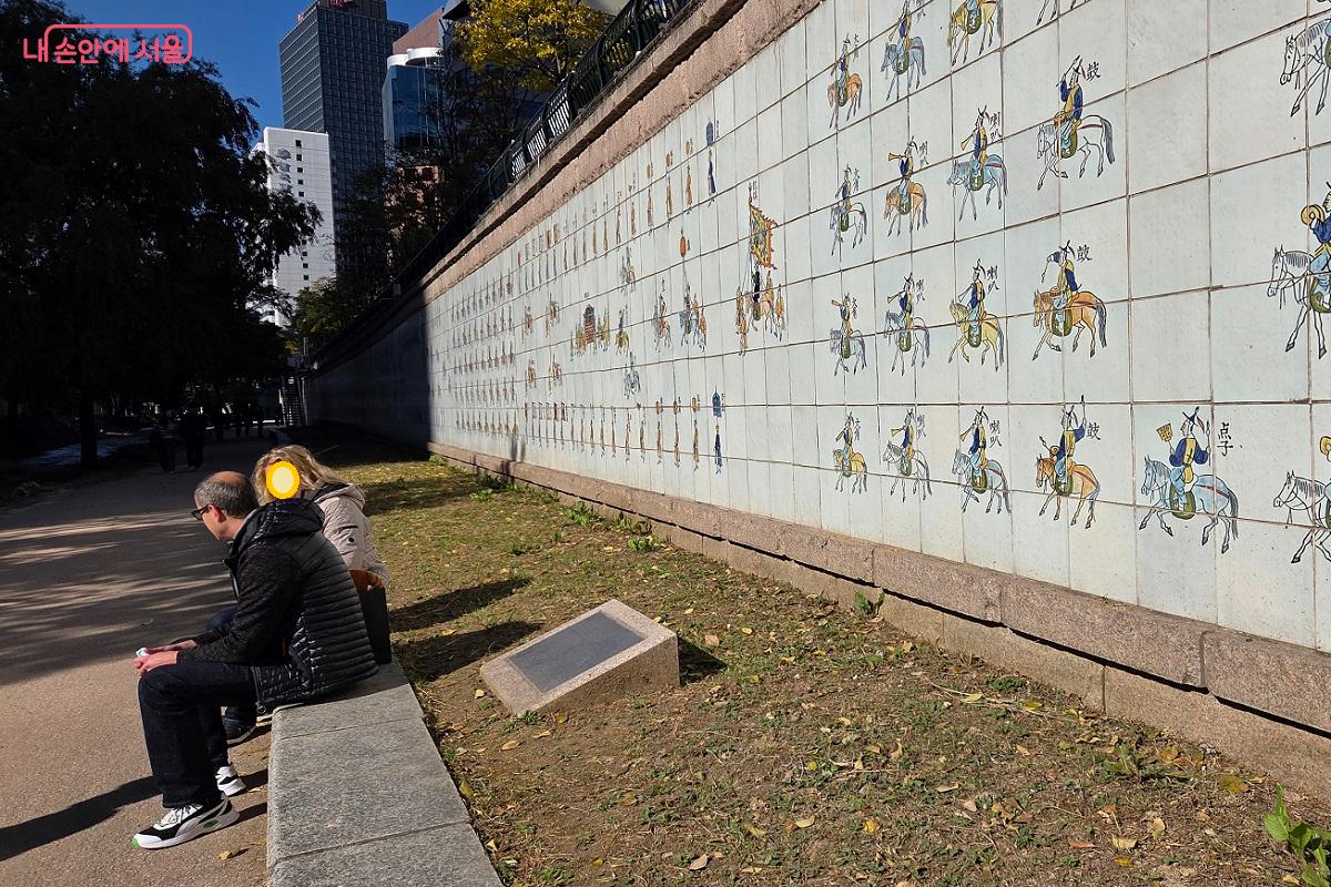 정조대왕 행차도가 그려져 있는 벽 앞에서 휴식을 취하고 있는 외국인 &copy;이상돈