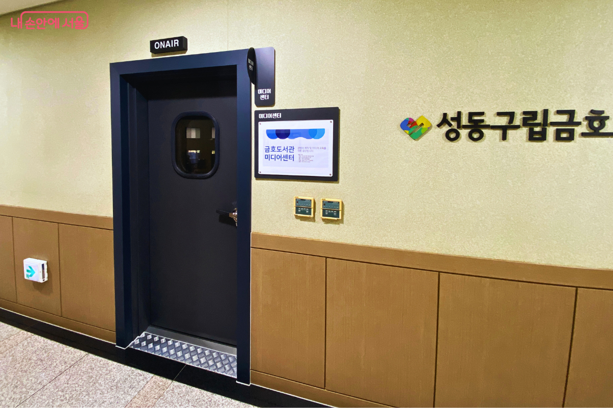 도서관 4층 복도 벽면에 설치된 '미디어센터'의 입구 모습이다. 'ON AIR' 사인이 달린 짙은 남색의 방음문이 닫혀 있고, 문 옆에는 '성동구립금호도서관 미디어센터' 현판이, 오른쪽 벽에는 도서관 로고가 붙어 있다. ©양정화