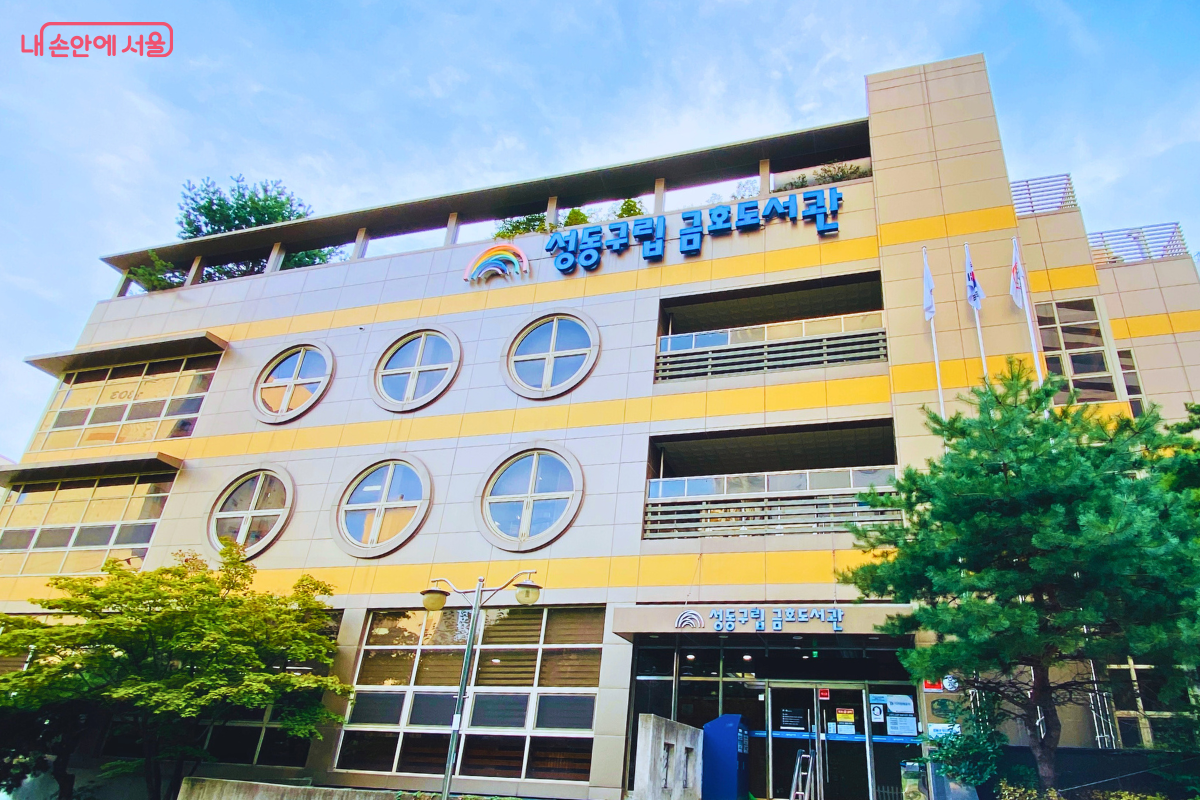 언덕 지형에 자리한 금호도서관의 정문 입구를 보여준다. '성동구립도서관' 간판이 붙은 유리문 입구가 1층이 아닌 건물 2층 높이에 바로 연결되어 있어, 경사지를 활용한 독특한 건축 구조를 알 수 있다. ©양정화