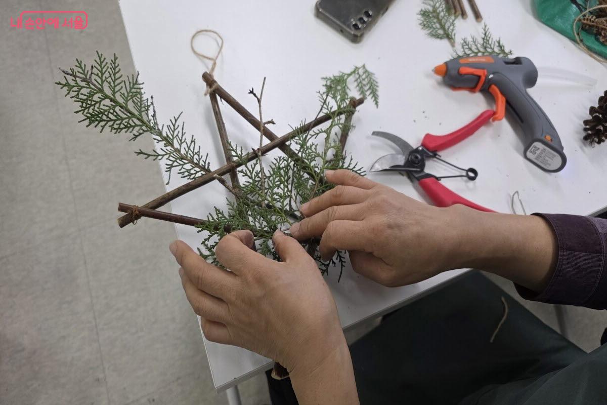 나뭇가지를 묶어 가며 오각형 별을 만들고 잎과 작은 장식물로 리스를 만들었다. ⓒ이선미 