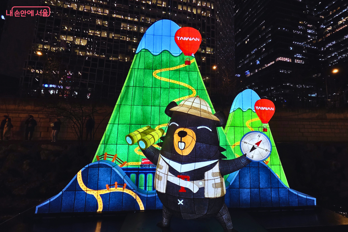 청계천 4구역에 설치된, 대만 관광을 홍보하는 마스코트 캐릭터 등불. 탐험가 모자와 조끼를 입은 대만 곰 캐릭터가 망원경과 나침반을 들고 서 있다. 뒤쪽 배경에는 푸른색과 녹색의 산과 산을 가로지르는 노란색 길이 표현되어 있으며, 산 위에는 'TAIWAN' 문구가 적힌 빨간색 열기구 조형물이 떠 있다. 이는 해외 국가 또는 도시가 참여하여 자국 문화를 홍보하는 조형물이다.
