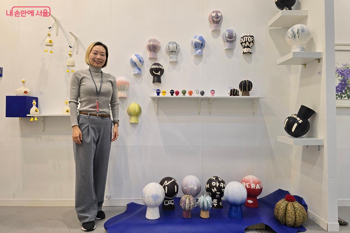 조아라 작가가 작품들 옆에 서서 환하게 웃고 있다. ©조성희