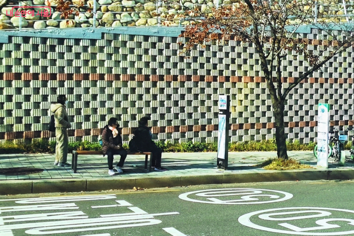 아파트 옹벽 앞 정류장에서 시민들이 벤치에 앉거나 서서 성공버스를 기다리고 있다. 질서 정연하게 버스를 기다리는 모습에서 성공버스가 지역 주민의 일상 속에 깊이 자리 잡았음을 확인할 수 있다. ©양정화