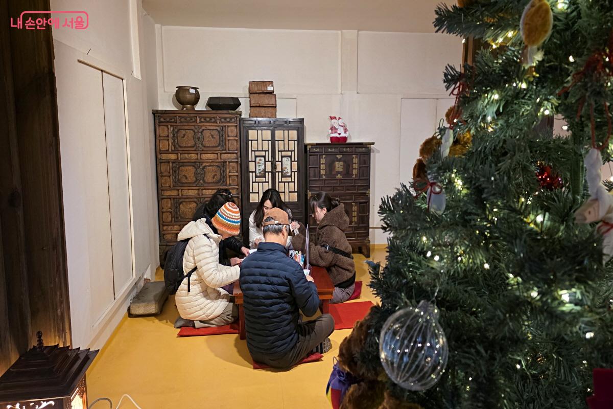 크리스마스 트리 너머 가족이 단란하게 체험에 참여하고 있다.ⓒ이선미