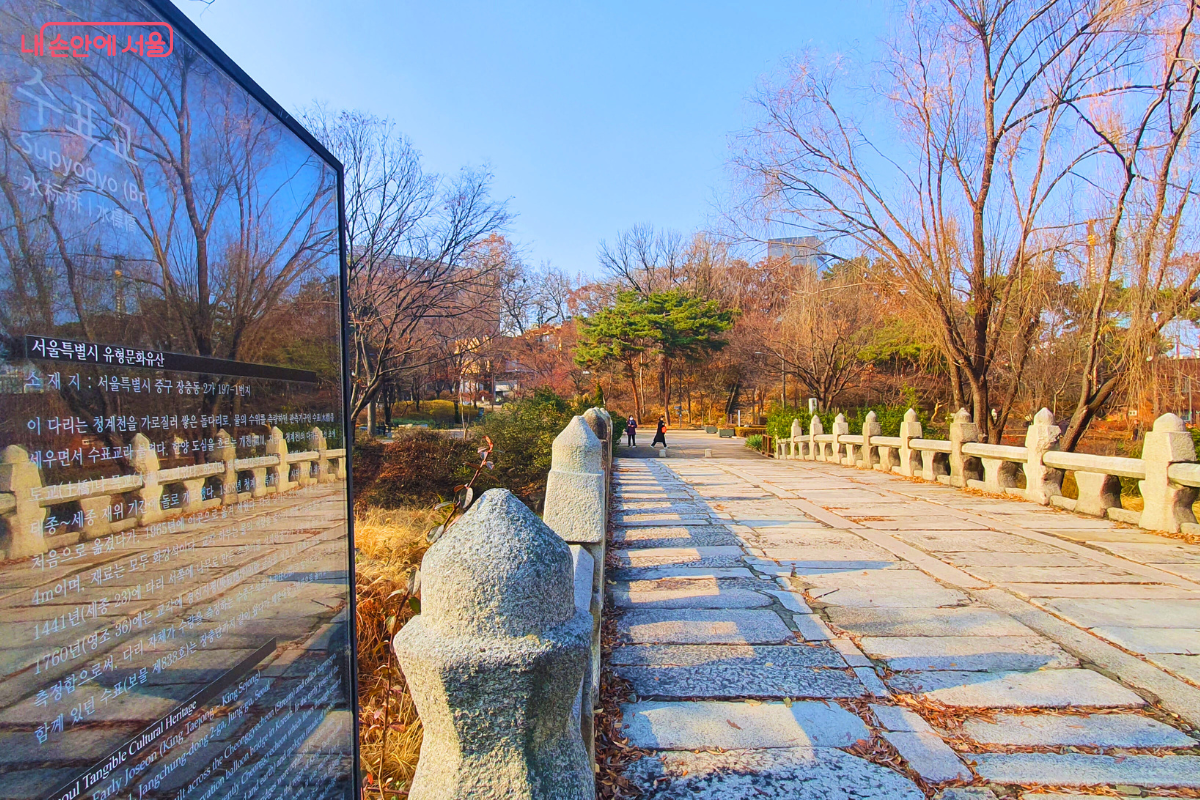 과거 청계천에 있었으나 현재 장충단공원으로 옮겨진 서울특별시 유형문화유산 수표교의 모습이다. 화강암으로 견고하게 쌓아 올린 돌다리의 바닥면과 독특한 모양의 난간석들이 길게 이어져 있다. 왼쪽 전경에는 수표교의 역사적 가치와 특징을 한글과 영어로 설명하는 커다란 유리 안내판이 세워져 있다. &copy;양정화