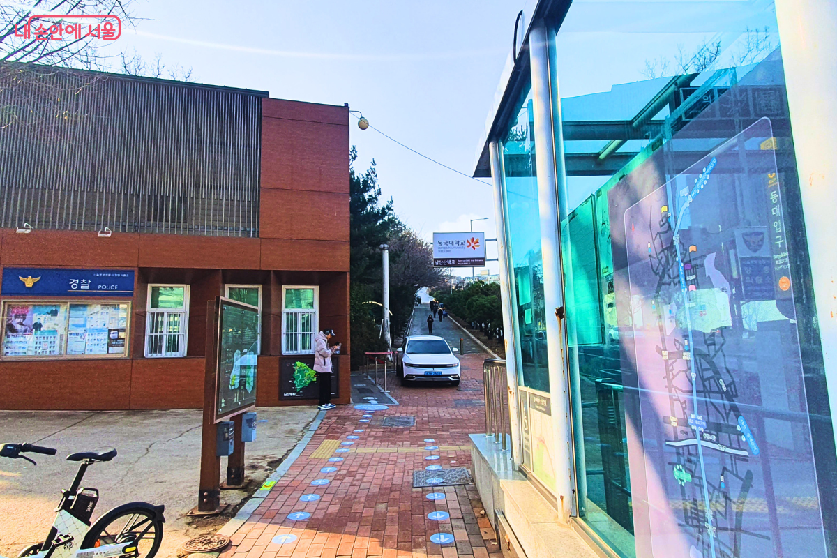 지하철 3호선 동대입구역 6번 출구 앞 보도의 전경이다. 화면 왼쪽에는 갈색 벽면의 장충파출소가 위치해 있고, 오른쪽에는 지하철역 출입구의 유리 구조물이 보인다. 멀리 동국대학교 입구와 남산 산책로를 알리는 표지판이 있다. &copy;양정화