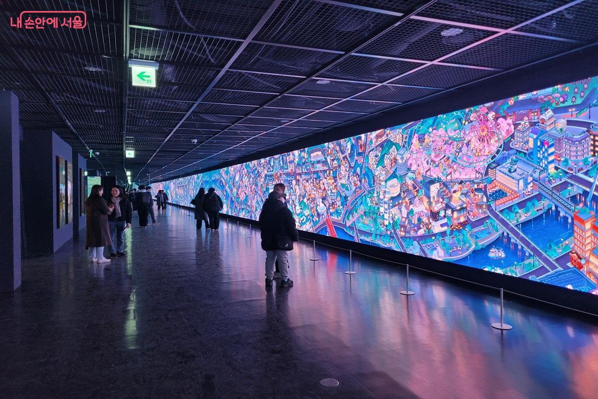 돈덕전 내부에 설치된 긴 대형 스크린에 화려한 일러스트 영상이 상영되고 있고 관람객들이 서서 감상하는 모습.